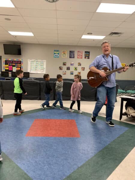 Adult playing guitar for children in a classroom