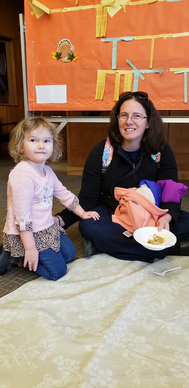 Adult and child sitting on the floor, adult holding a plate of food