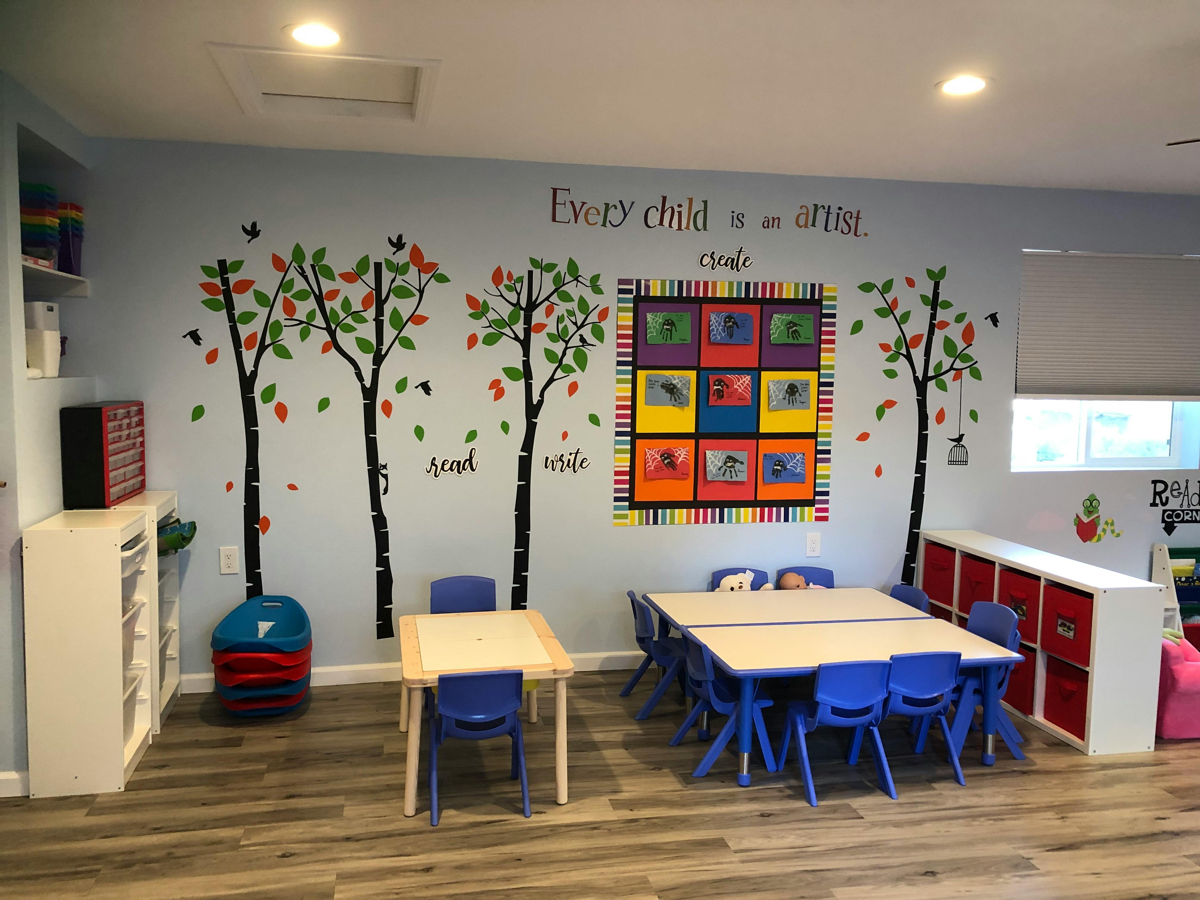 Classroom with tables and chairs, tree decals on wall, and colorful artwork
