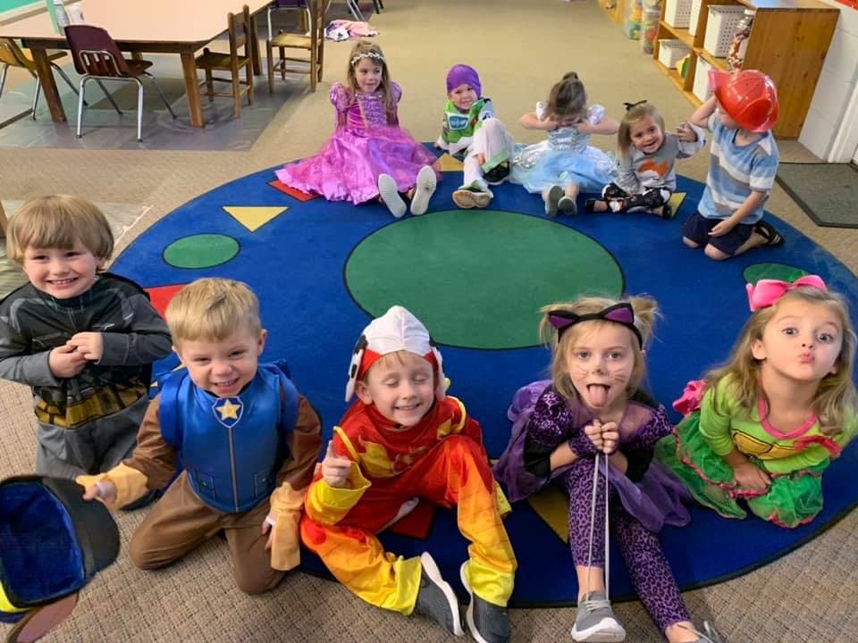 Children in costumes sitting on a colorful rug in a classroom