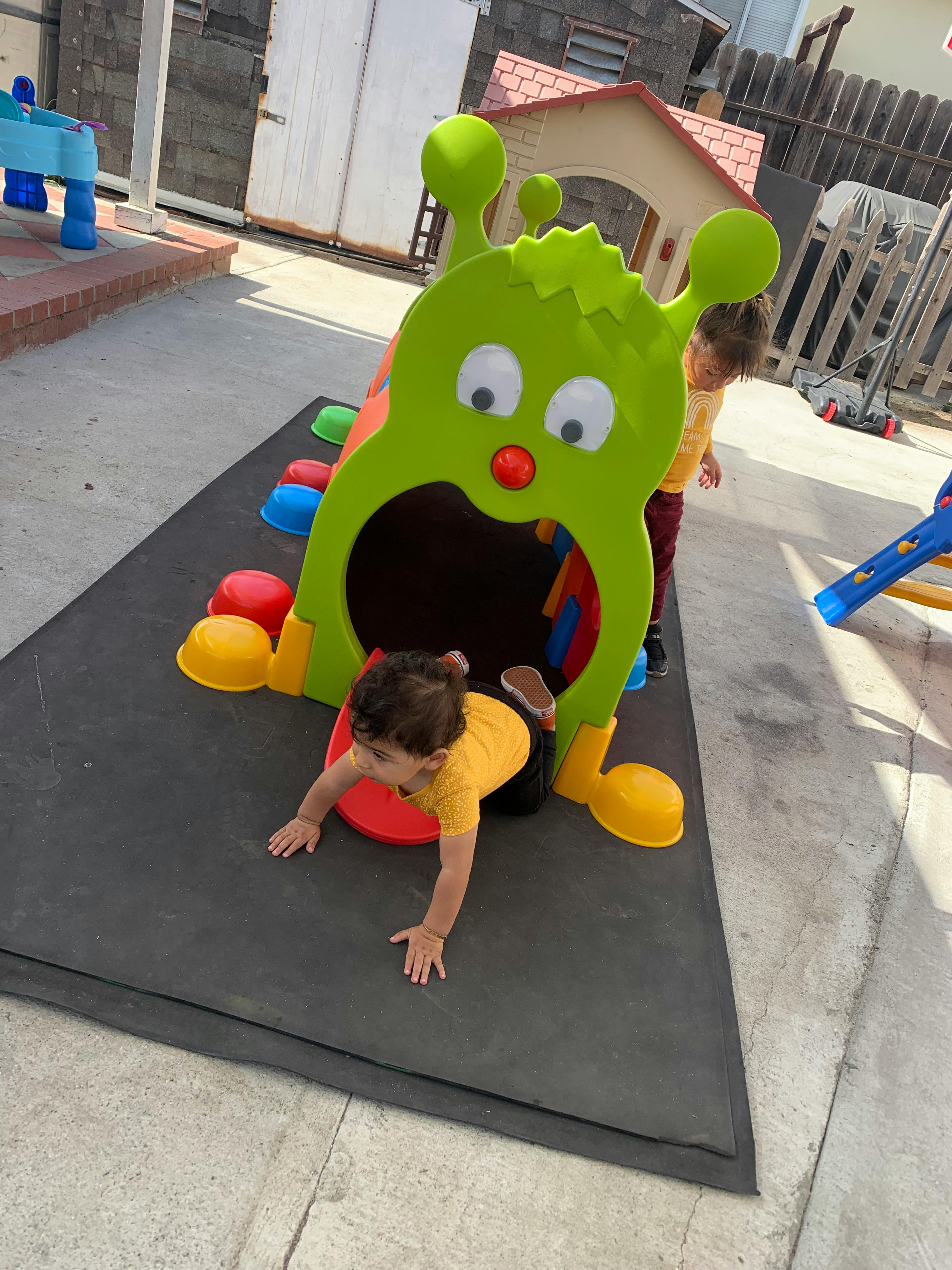 Child crawling out of a green monster-shaped play tunnel