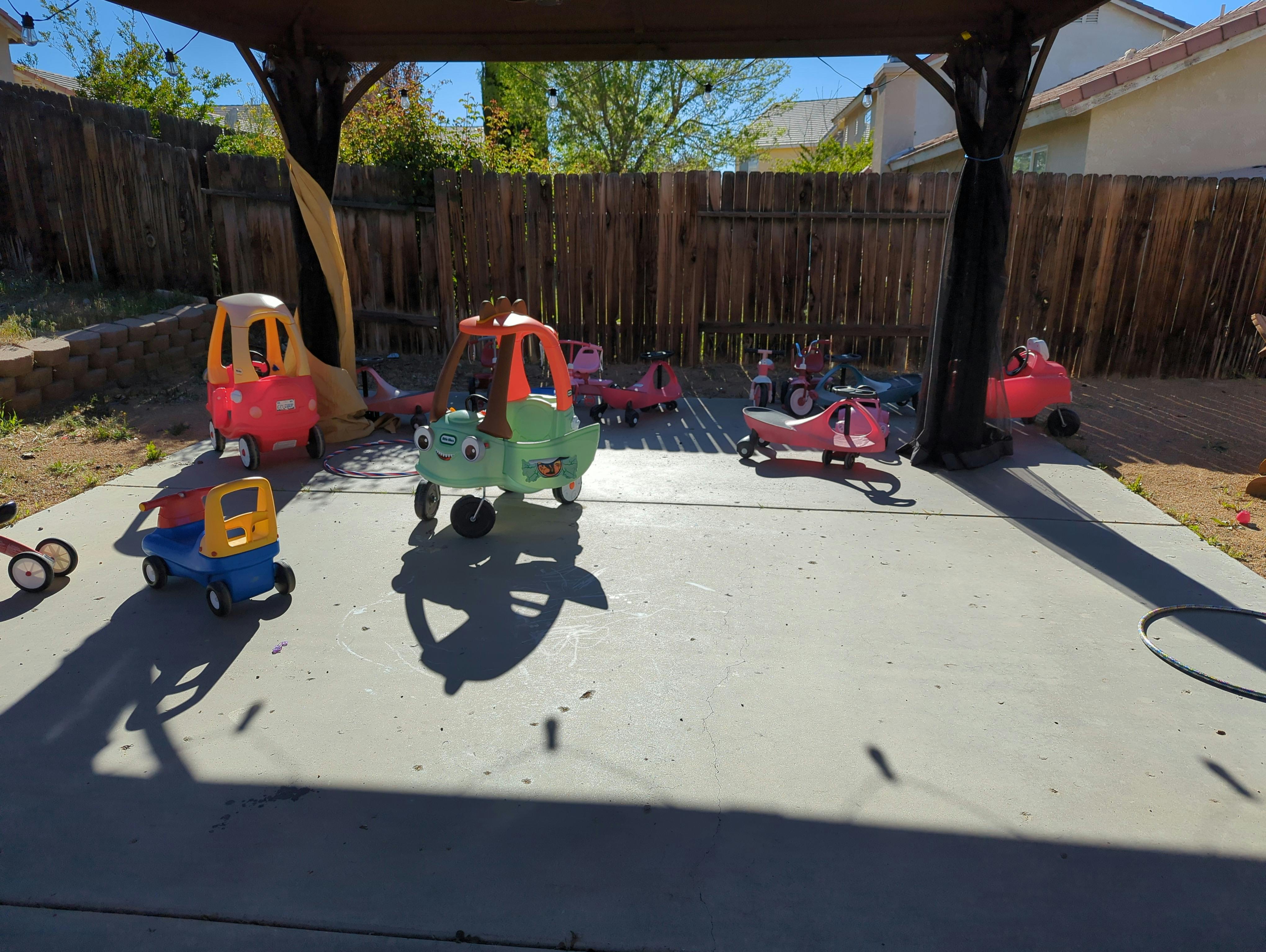 Multiple toy cars and tricycles on a paved area