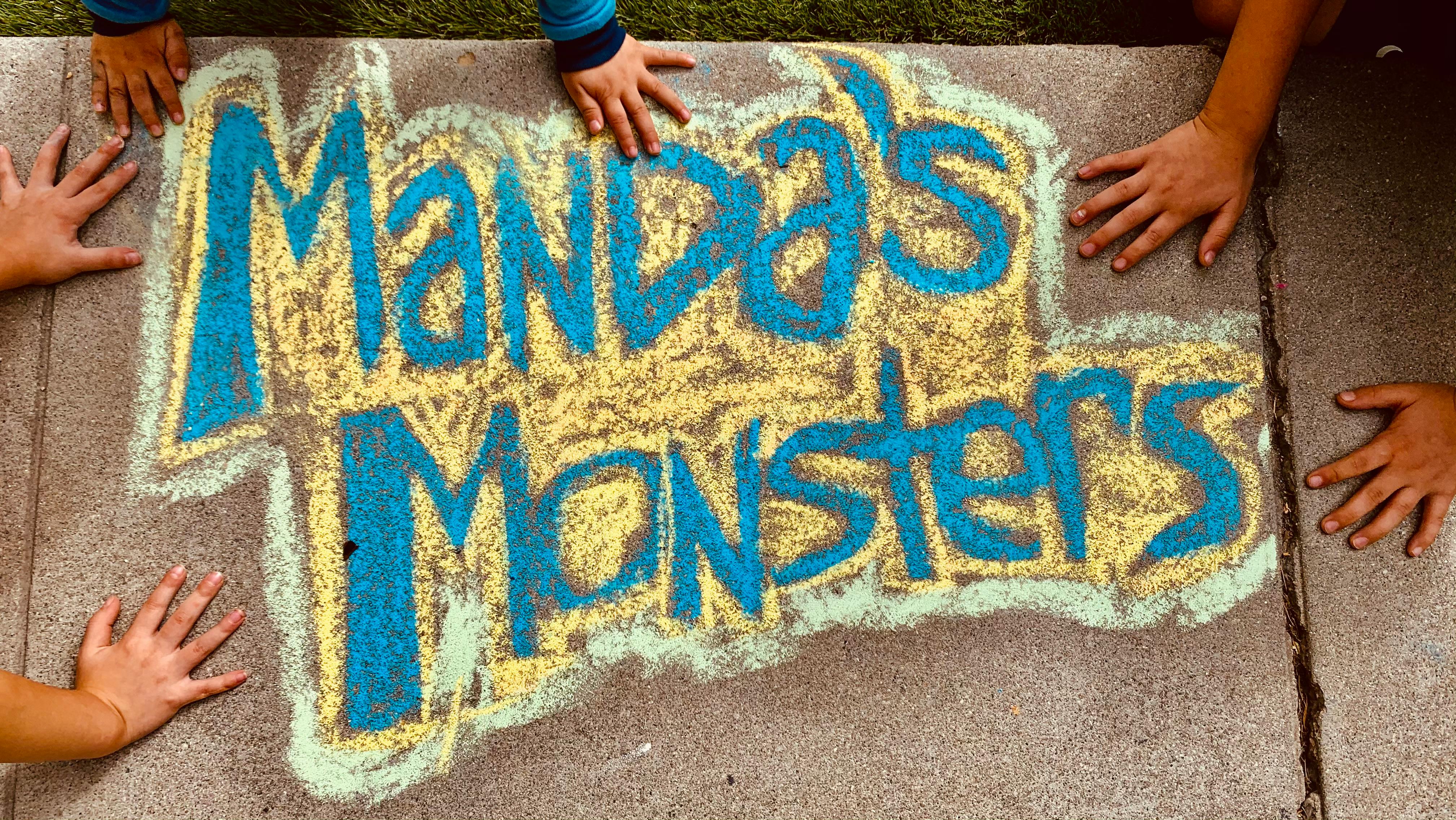 Chalk drawing on pavement that says "Manda's Monsters" with children's hands around it