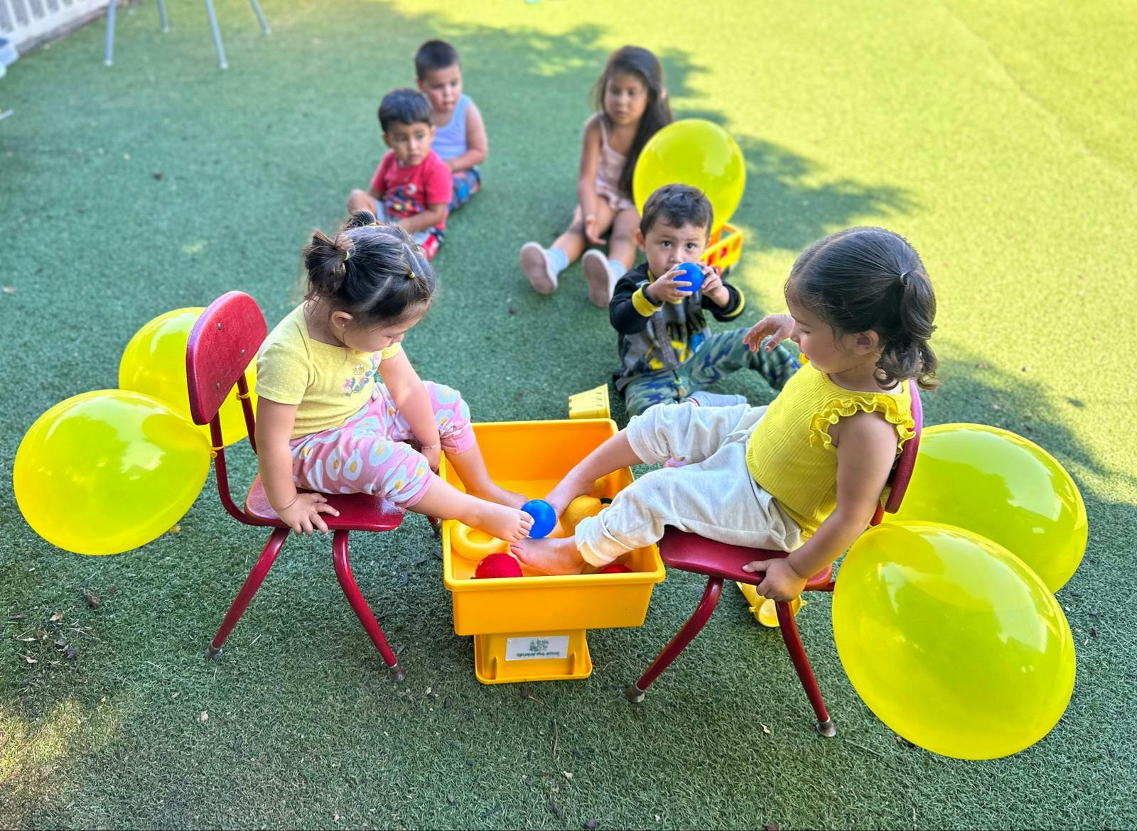 Children playing with water in a yellow bin outdoors