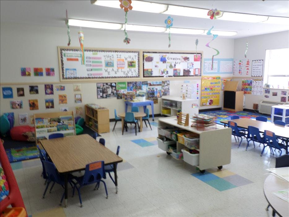 An empty early childhood classroom with small tables, chairs, and learning materials