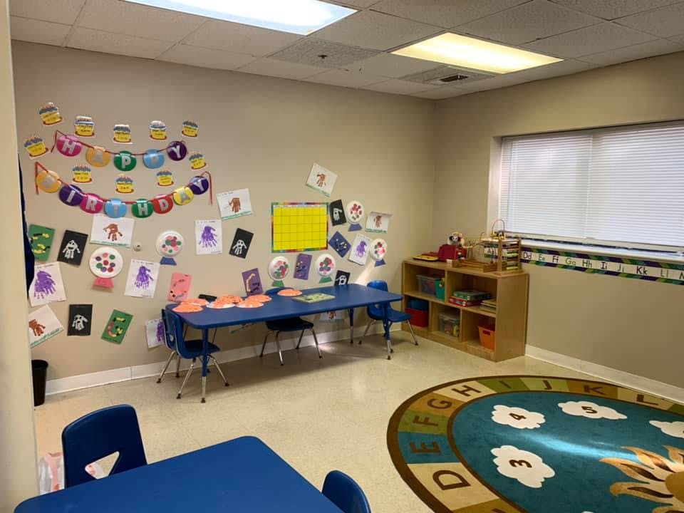 Classroom with children's artwork on the wall and small blue tables and chairs