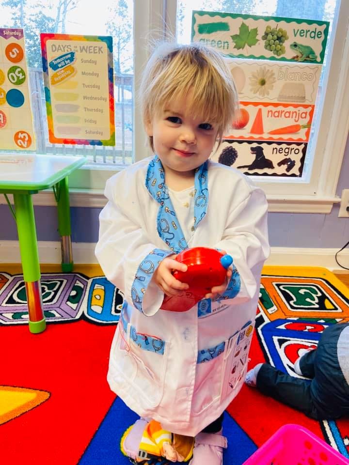 Child in a white lab coat holding a red toy