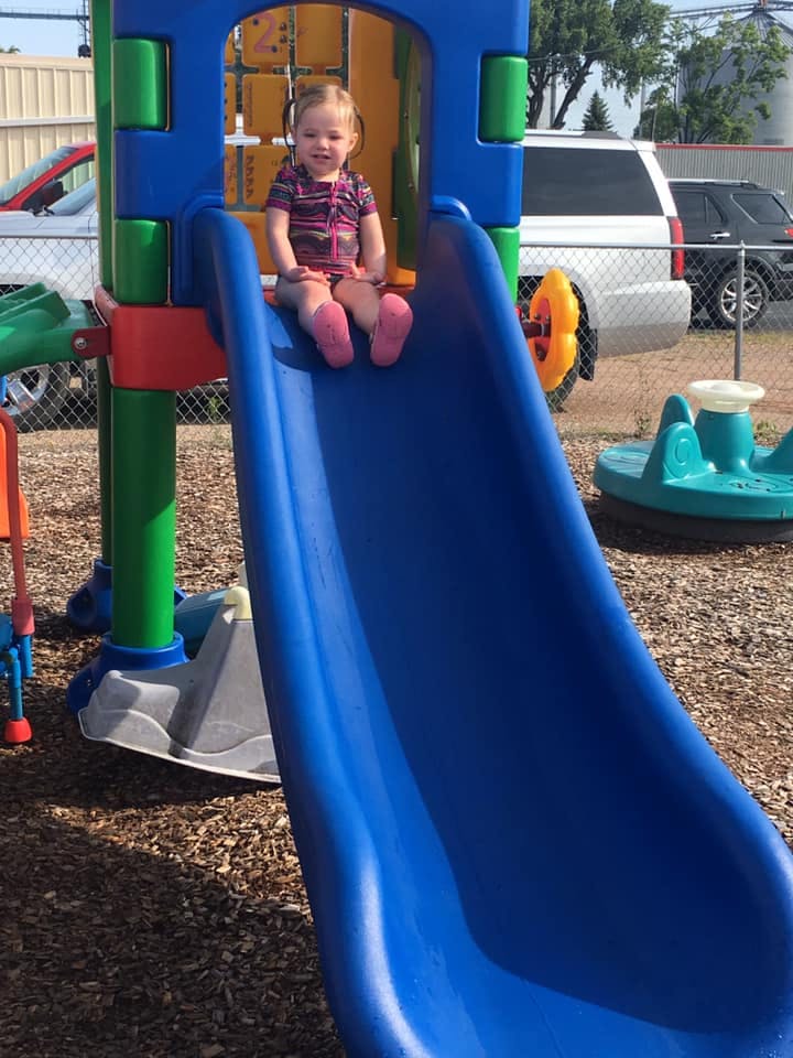 Child sitting at the top of a blue slide on a playground