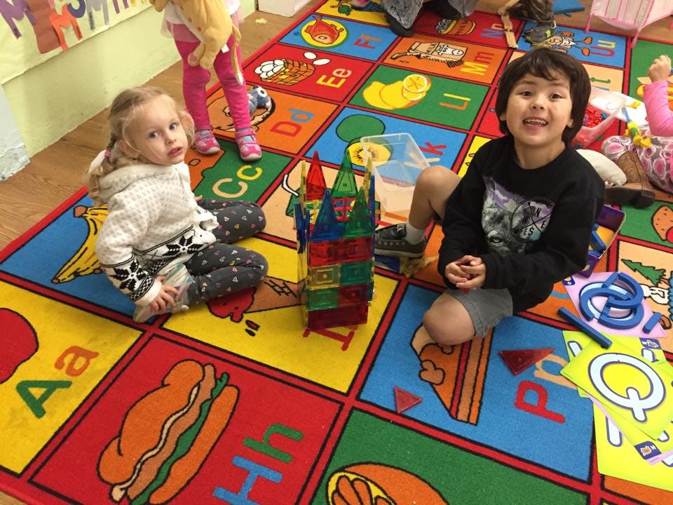 Two children playing on a colorful alphabet rug with building blocks