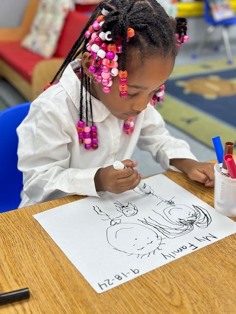 Child drawing a family picture on paper in a classroom