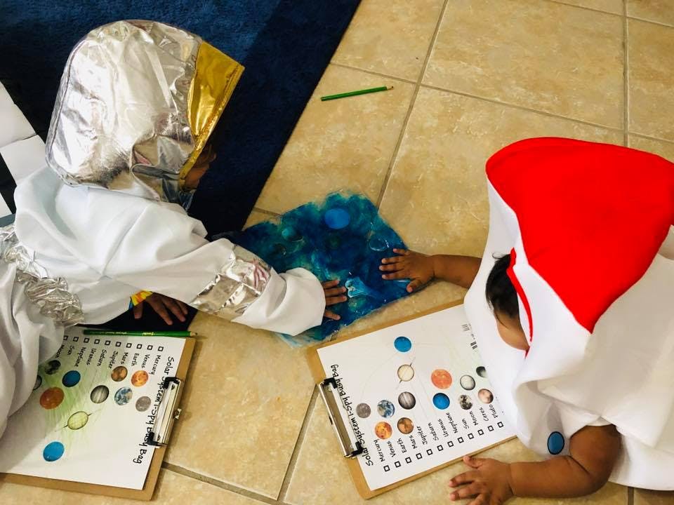 Two children in costumes playing with clipboards on the floor