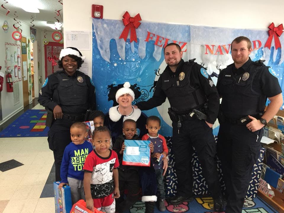Three police officers and several children posing for a photo indoors