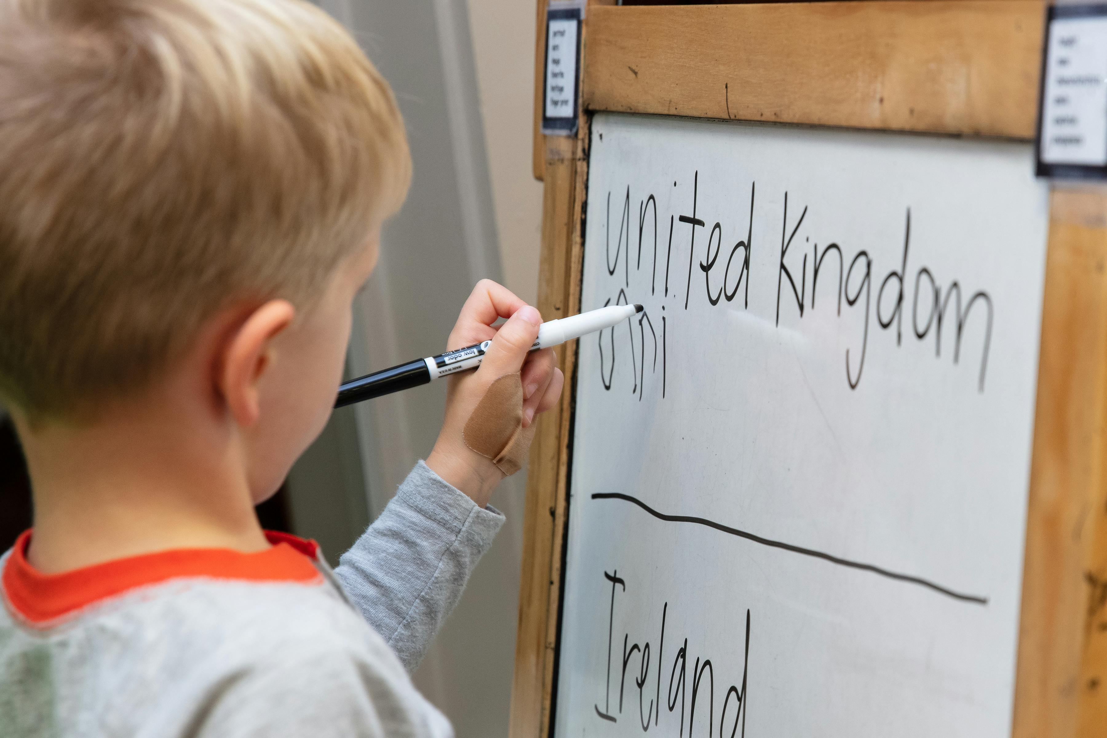 Child writing "United Kingdom" on a whiteboard
