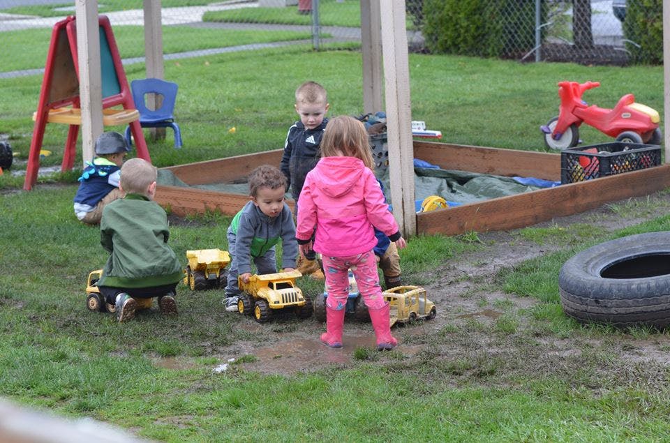 Children playing with toy trucks in a muddy outdoor area