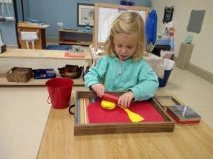 Child using a tool to cut a yellow object on a red mat