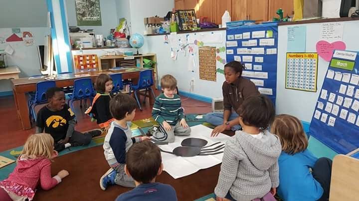 Adult and children sitting on floor in classroom looking at objects