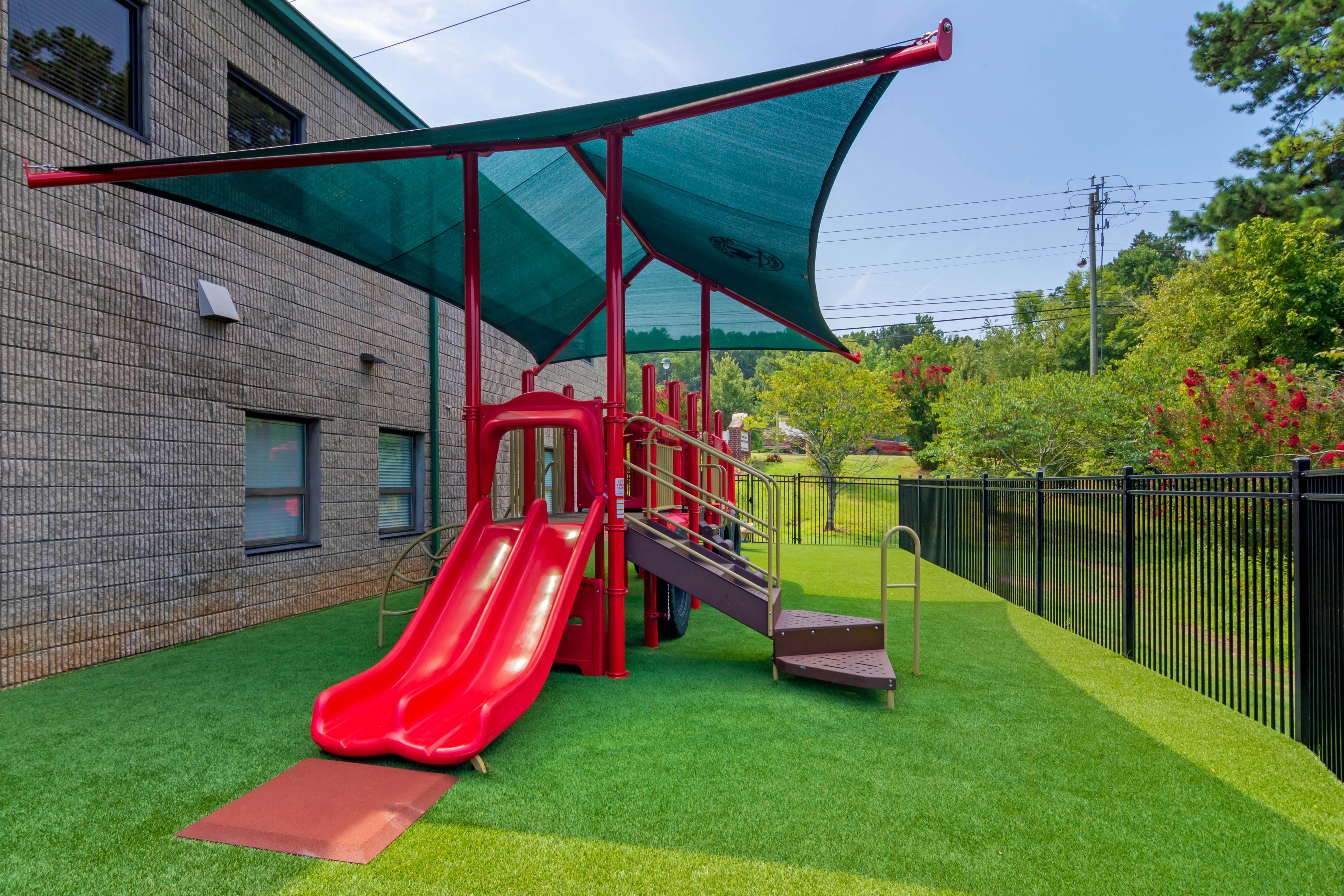 Red playground with a double slide and stairs under a green sunshade
