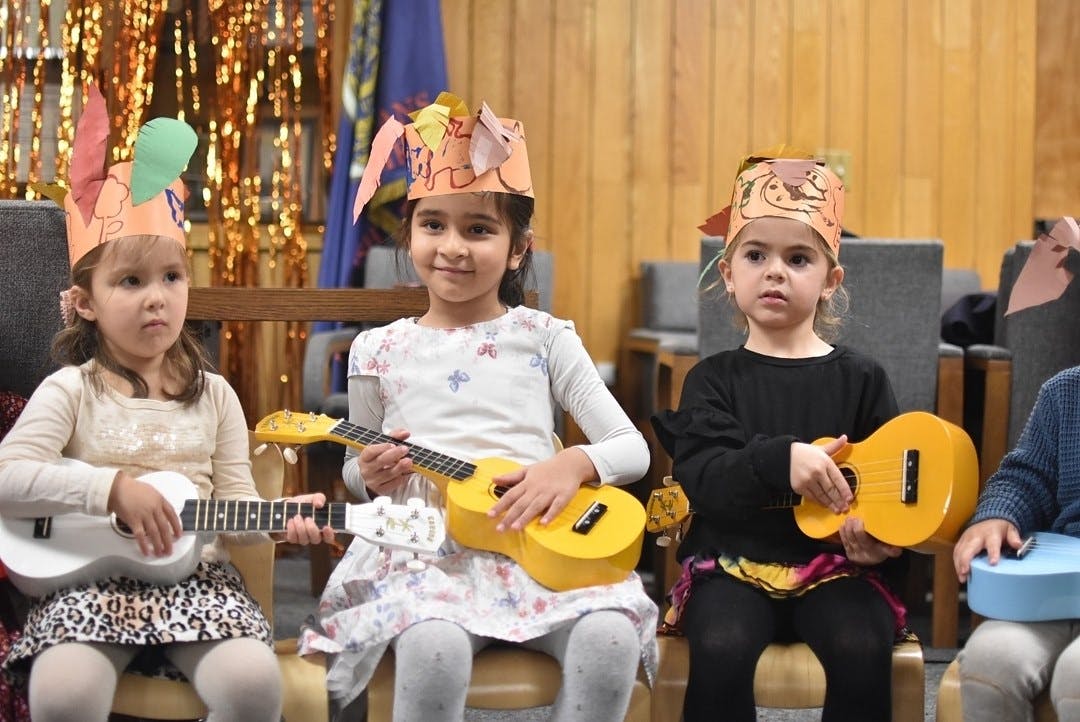 Three children wearing paper crowns and holding toy ukuleles
