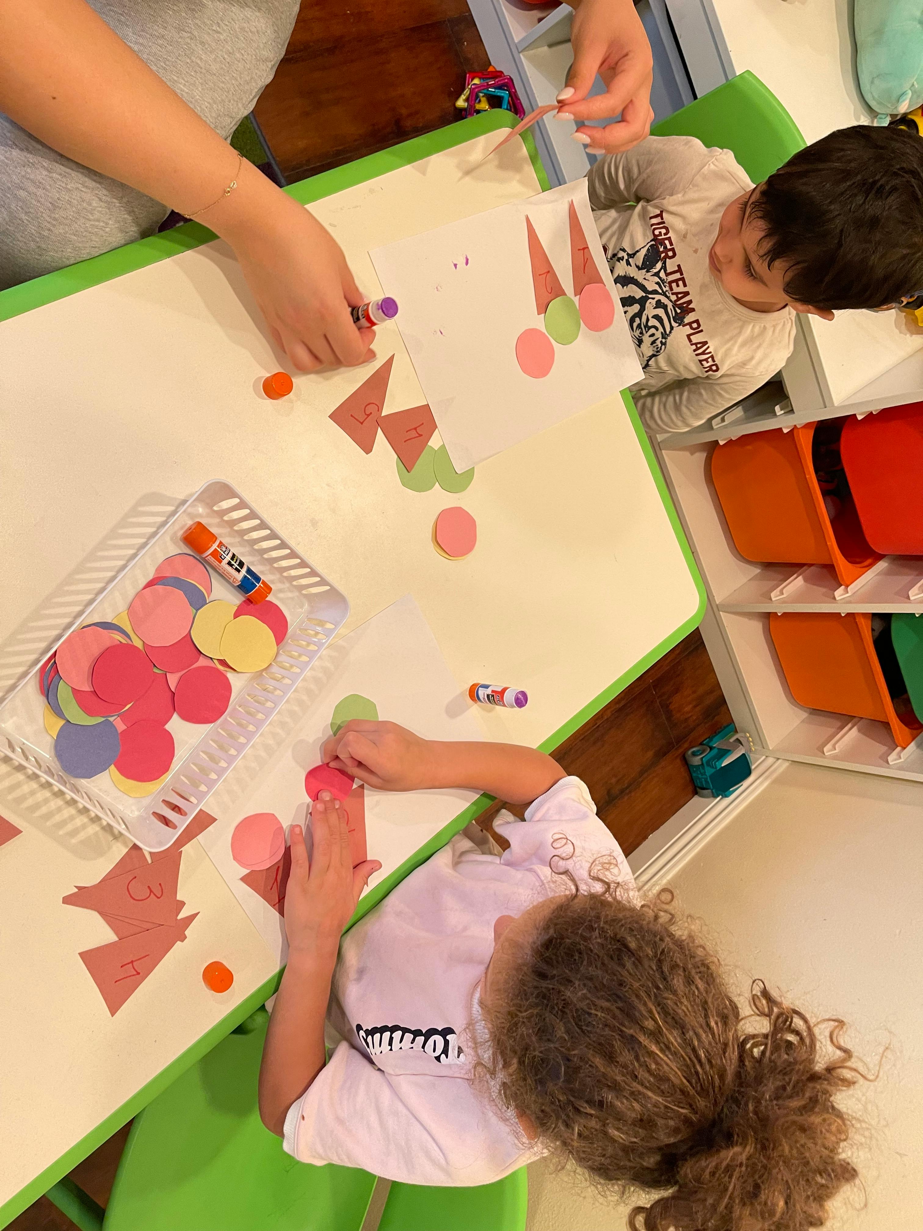 Two children and an adult doing a craft with paper cutouts and glue sticks