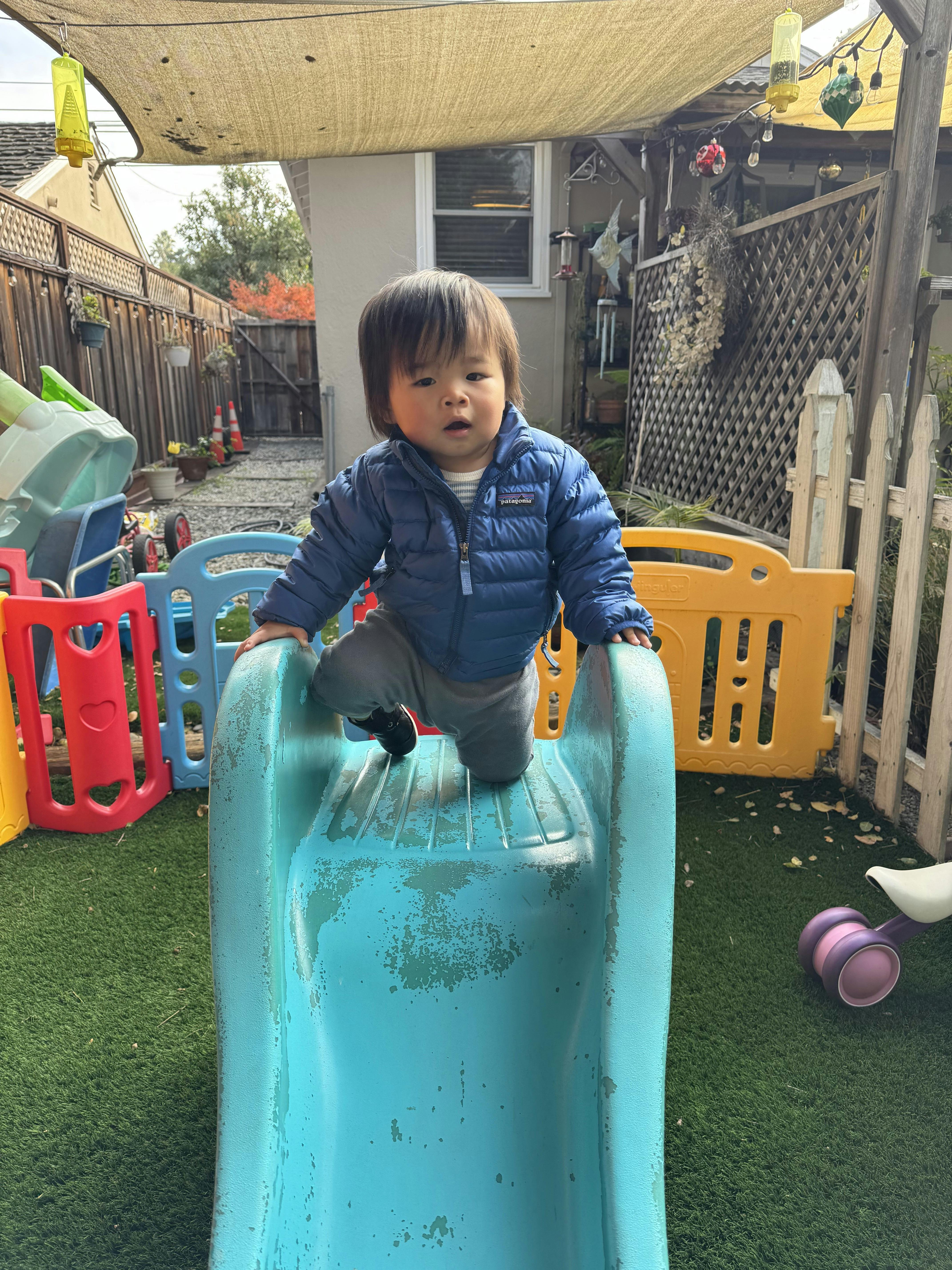 Child in a blue jacket kneeling at the top of a small blue slide