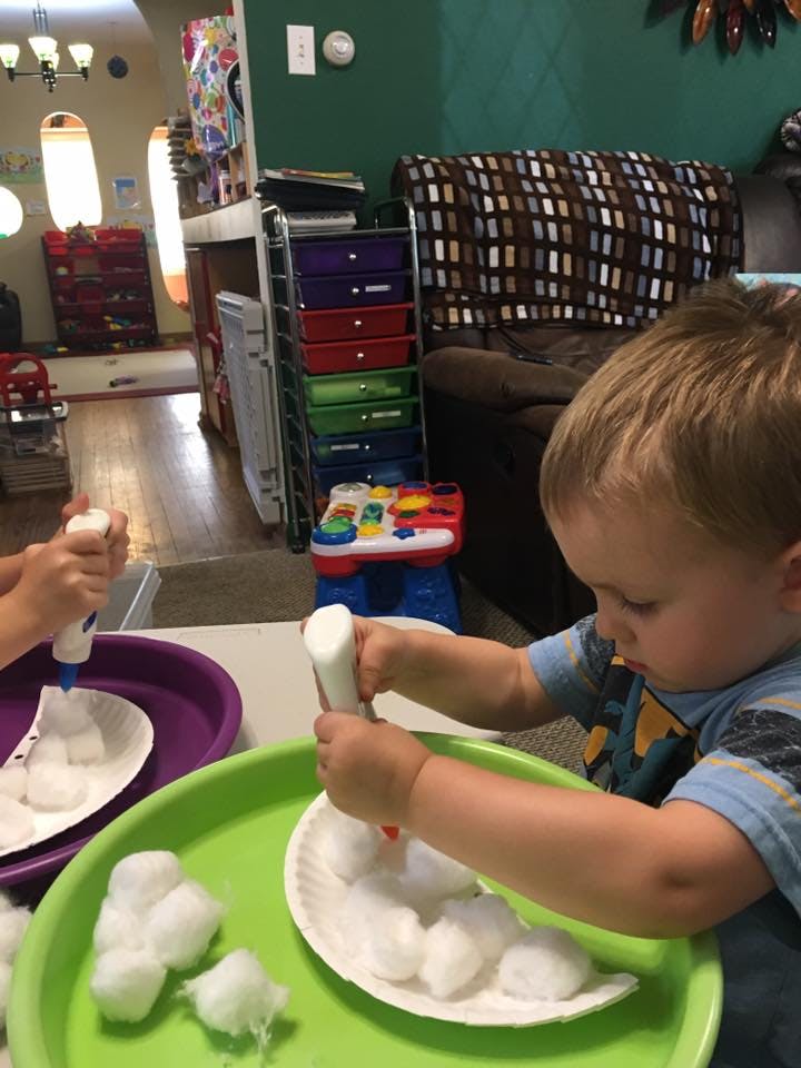 Child applying glue to cotton balls on a paper plate