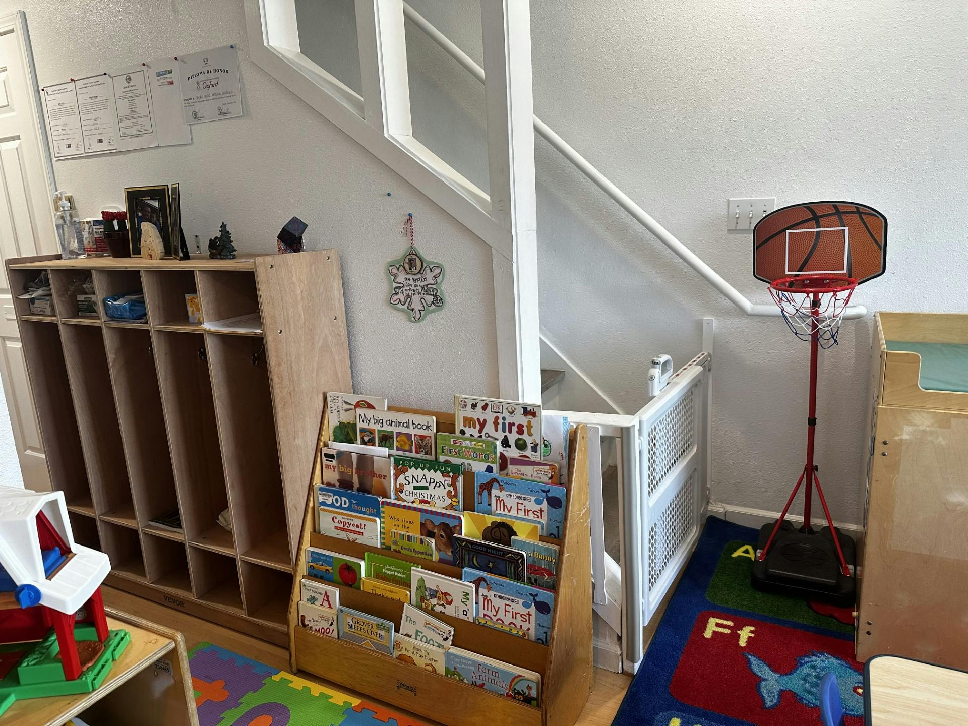 Children's books in a wooden display rack next to a cubby shelf and a toy basketball hoop
