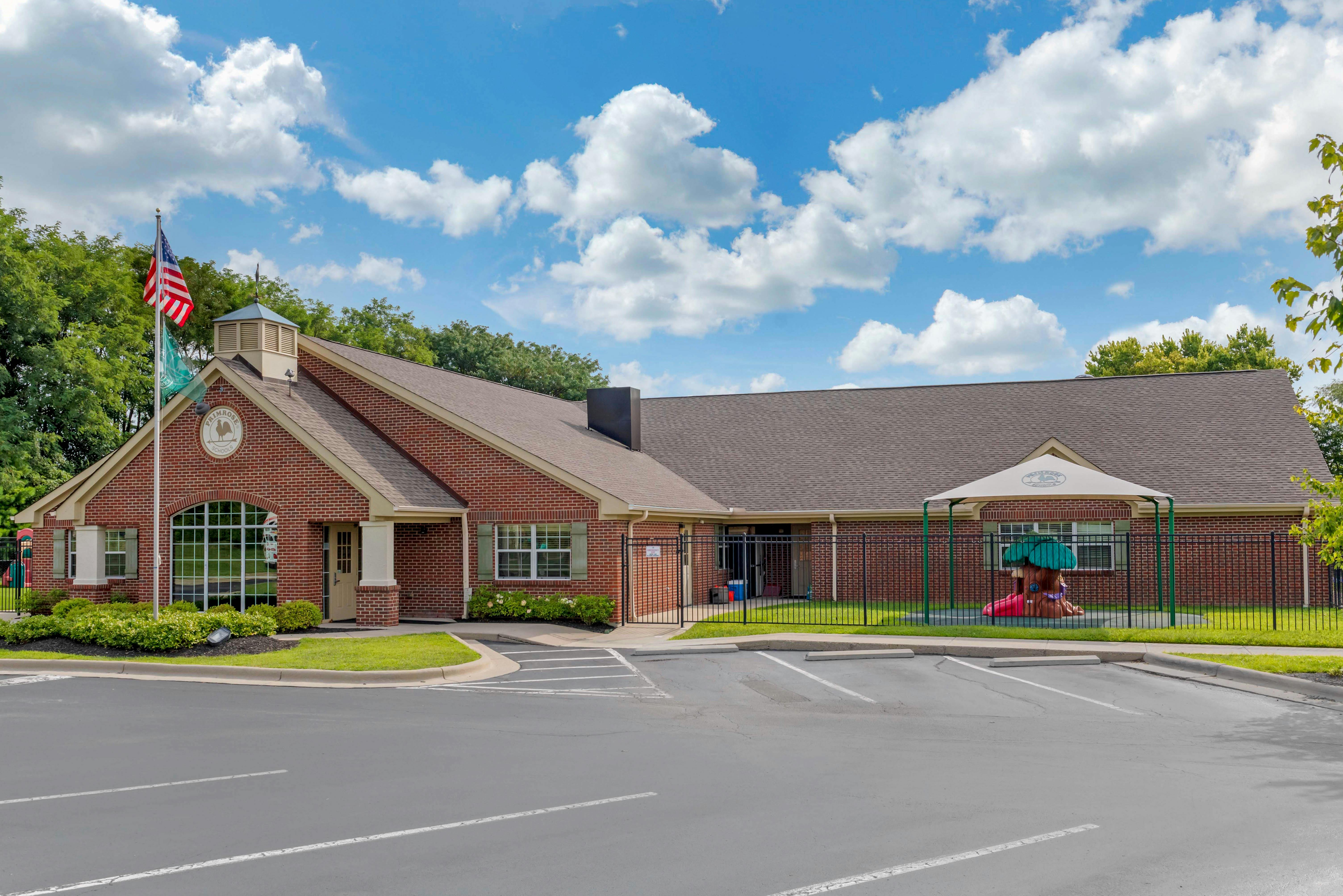 Brick school building with an American flag and a playground behind a fence