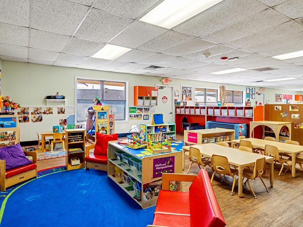 Empty classroom with small tables, chairs, and play areas