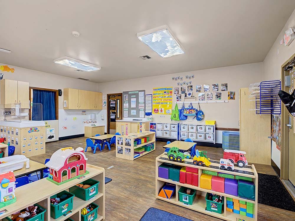 Empty colorful classroom with small tables and chairs, toys on shelves