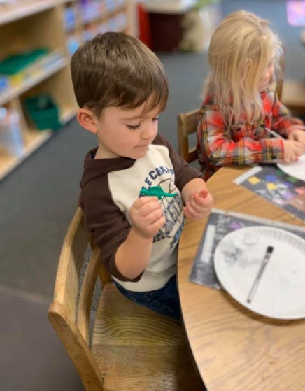 Child sitting at a table with another child, looking at hands