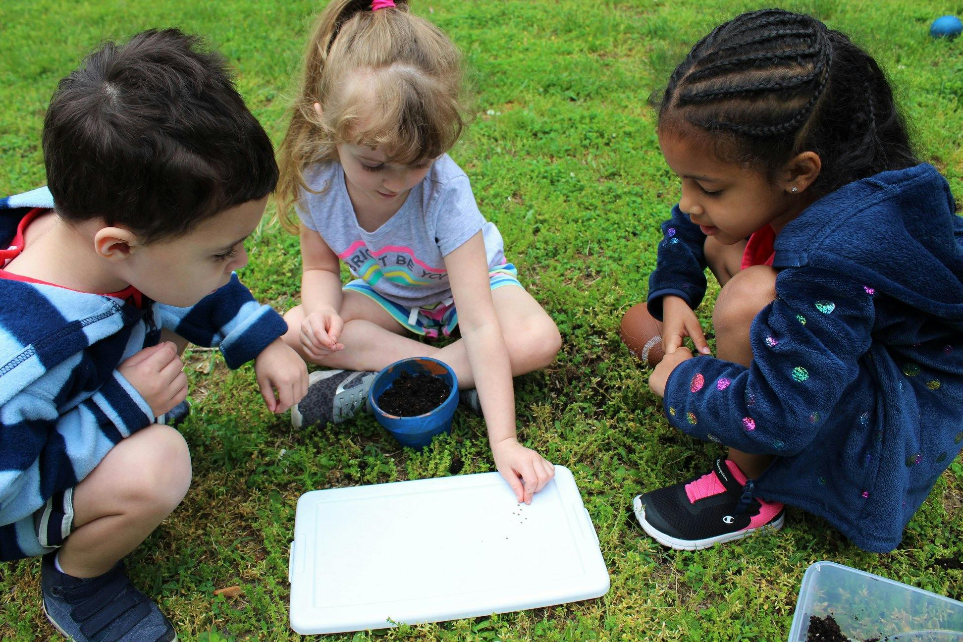 Three children on grass looking at a white tray