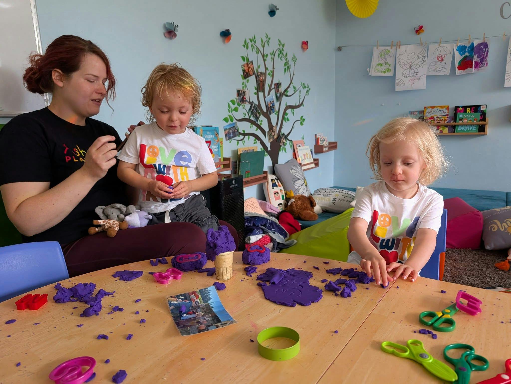 Person and two children playing with purple playdough at a table