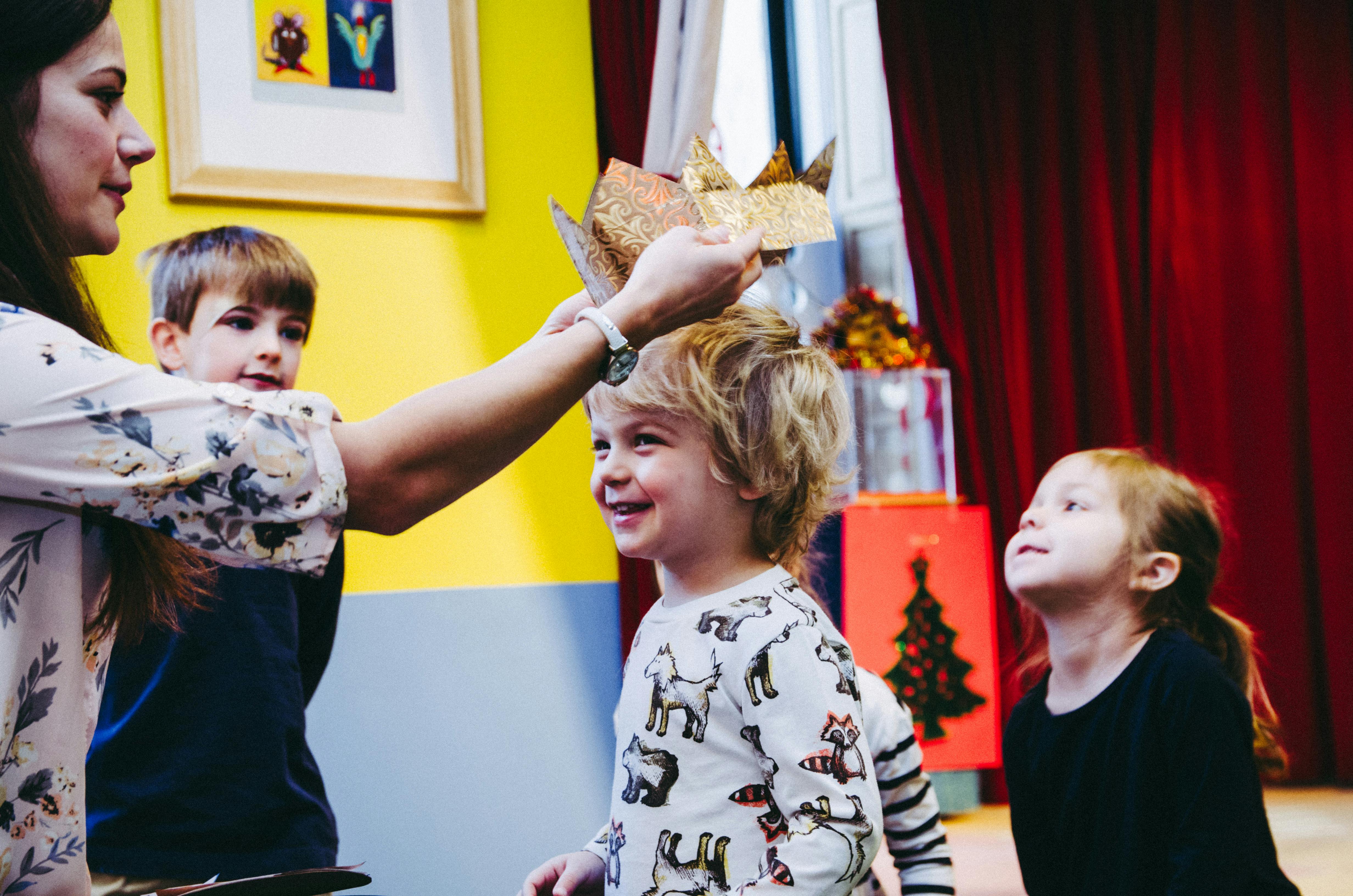 Person placing a crown on a child's head, with two other children watching