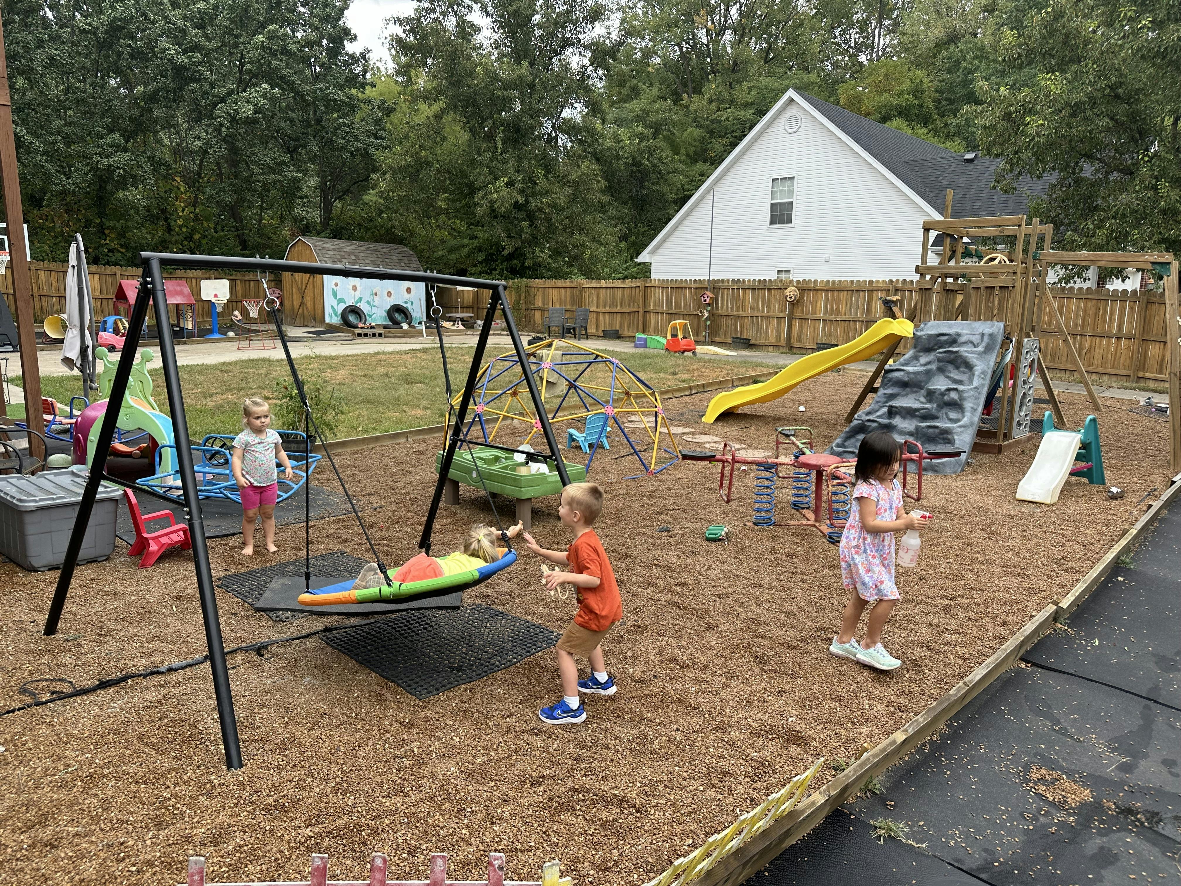 Children playing on a playground with a swing, slide, and climbing dome