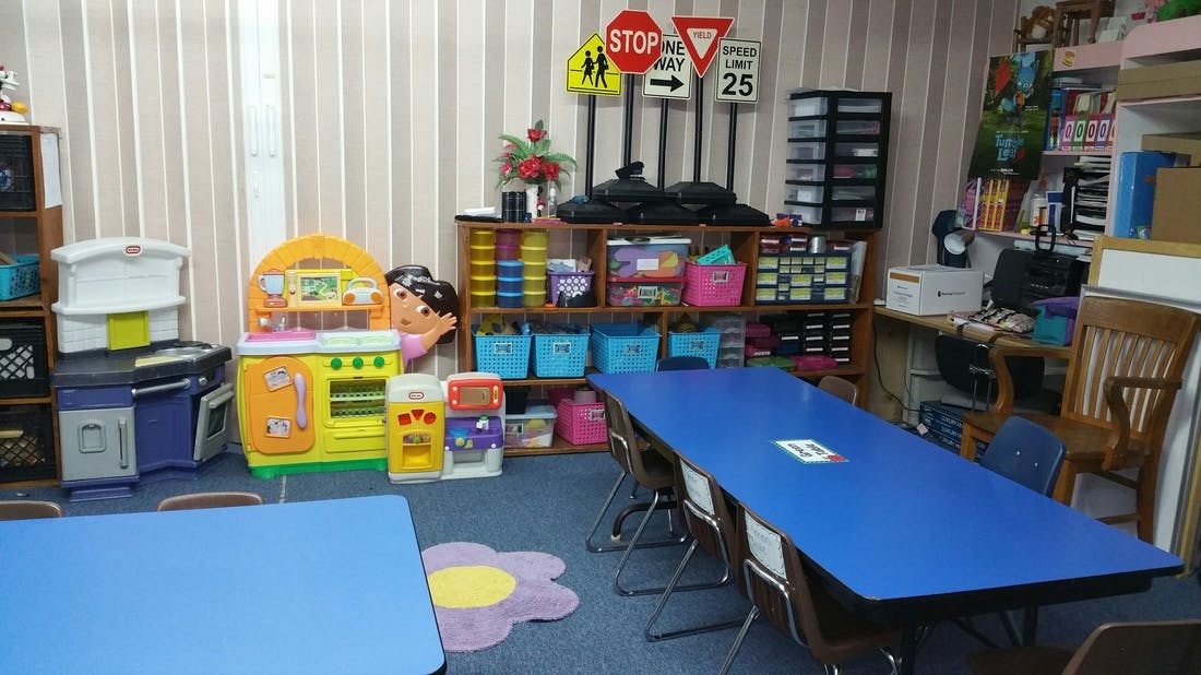 Classroom with blue tables, play kitchen, and shelves with toys