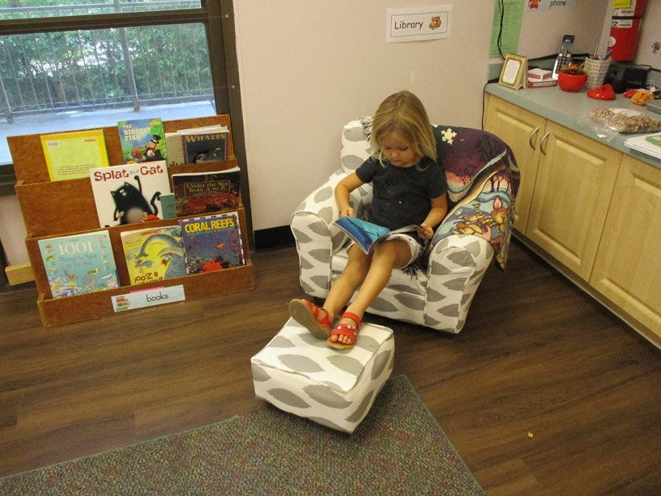 Child sitting in a chair reading a book in a classroom