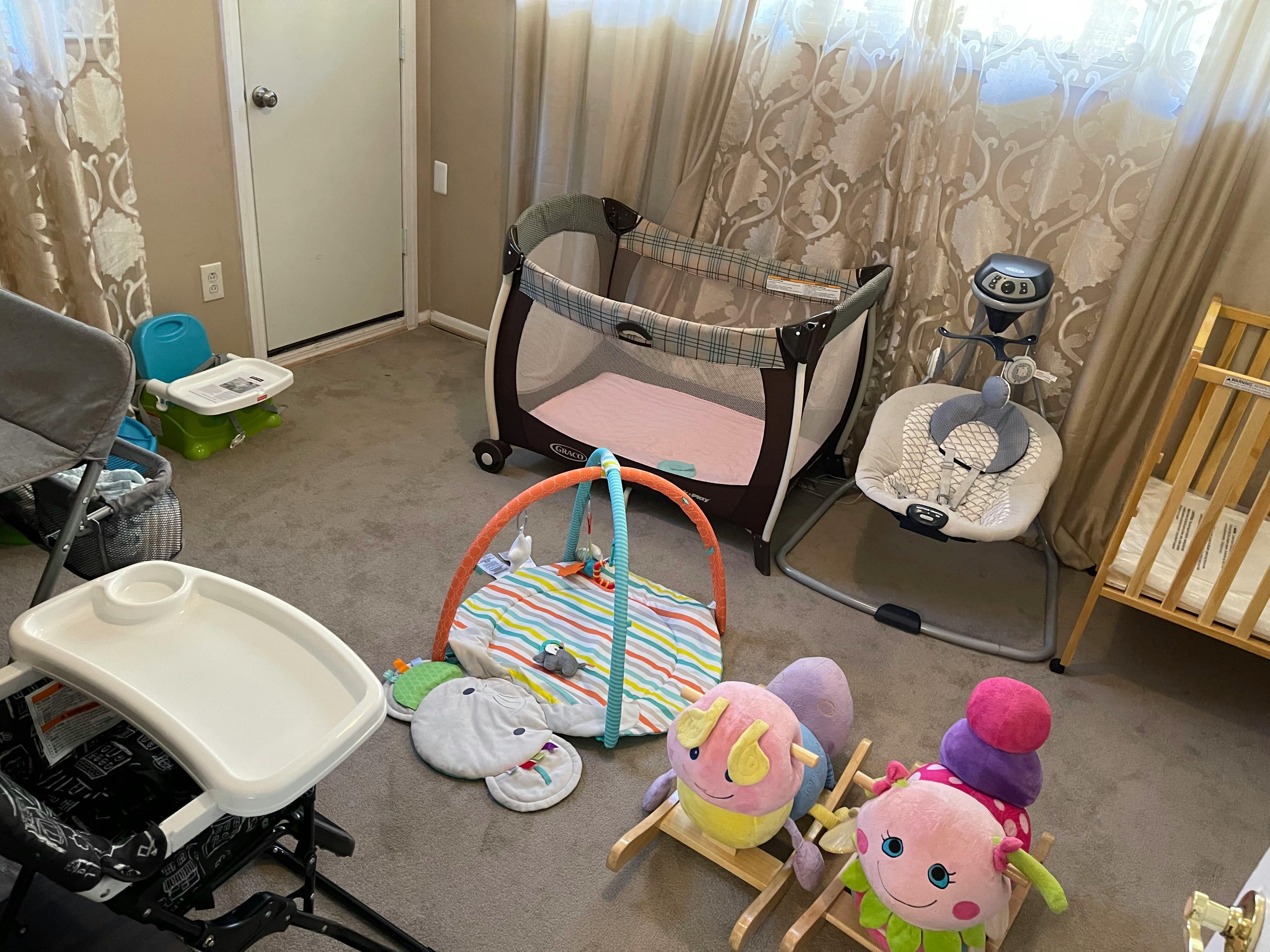 Baby playpen, bouncer, and play mat with toys in a room