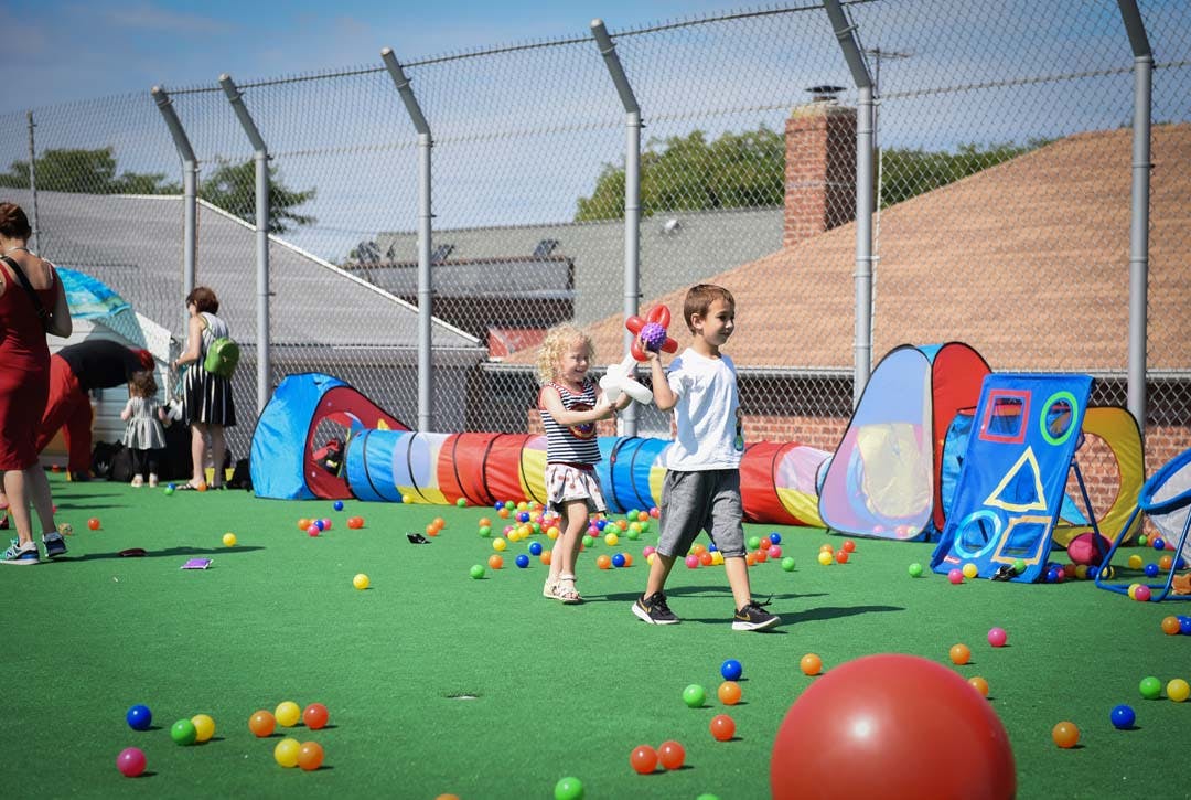 Two children playing with toys on a green turf with colorful balls