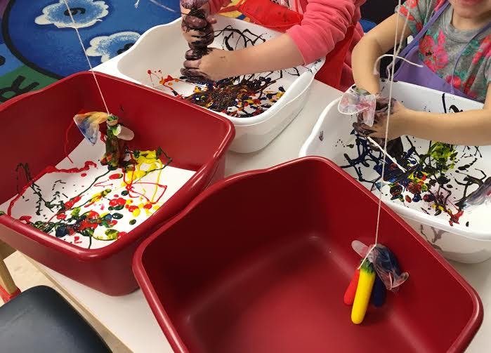 Children making art with paint and string in containers