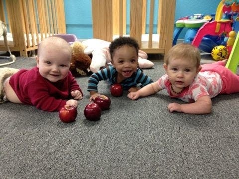 Three babies crawling on a carpeted floor with apples
