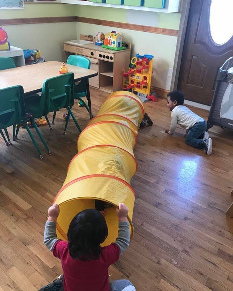 Child entering a yellow play tunnel while another child crawls nearby