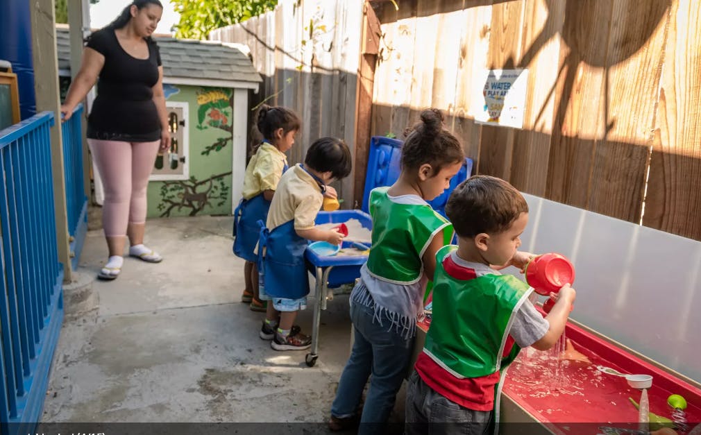 Adult supervising children playing with water at a table