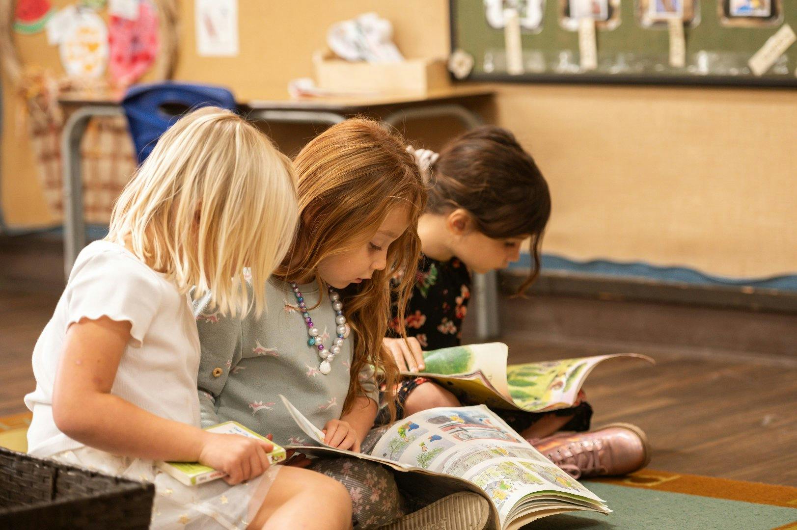 Three children sitting on a classroom floor reading books