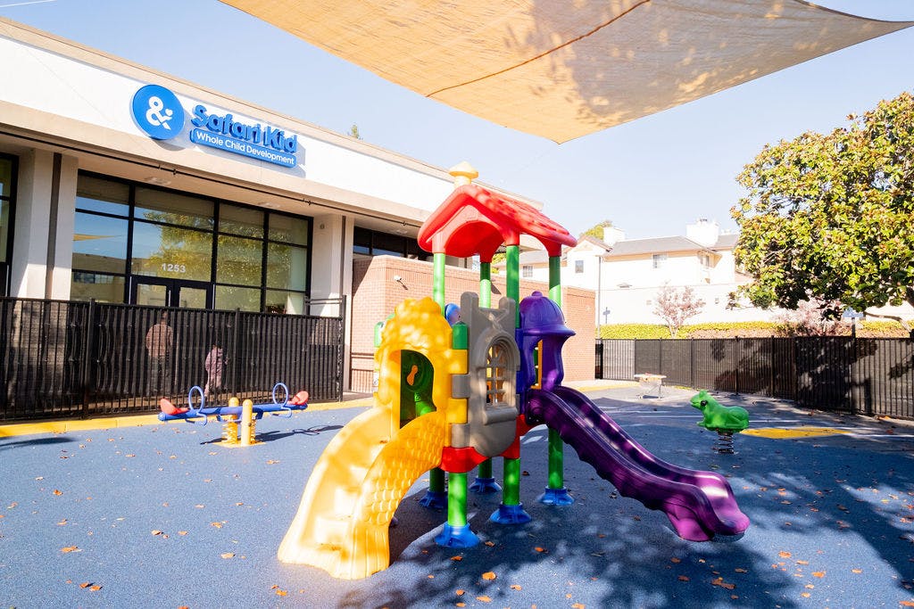 Colorful playground structure with slides and a seesaw outside a building