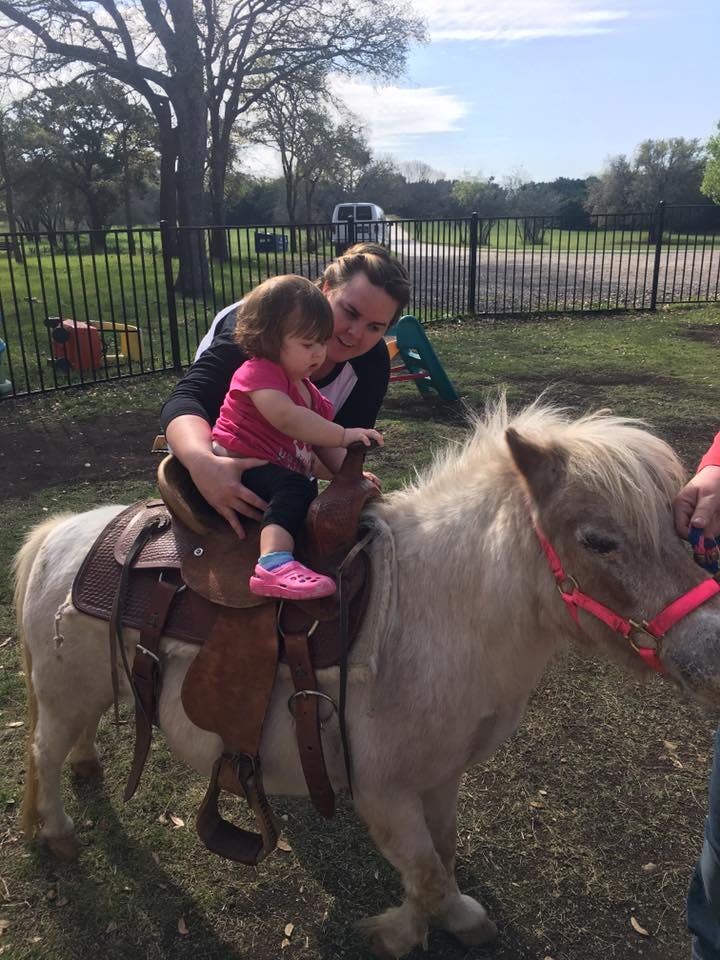 Person helping a child sit on a pony
