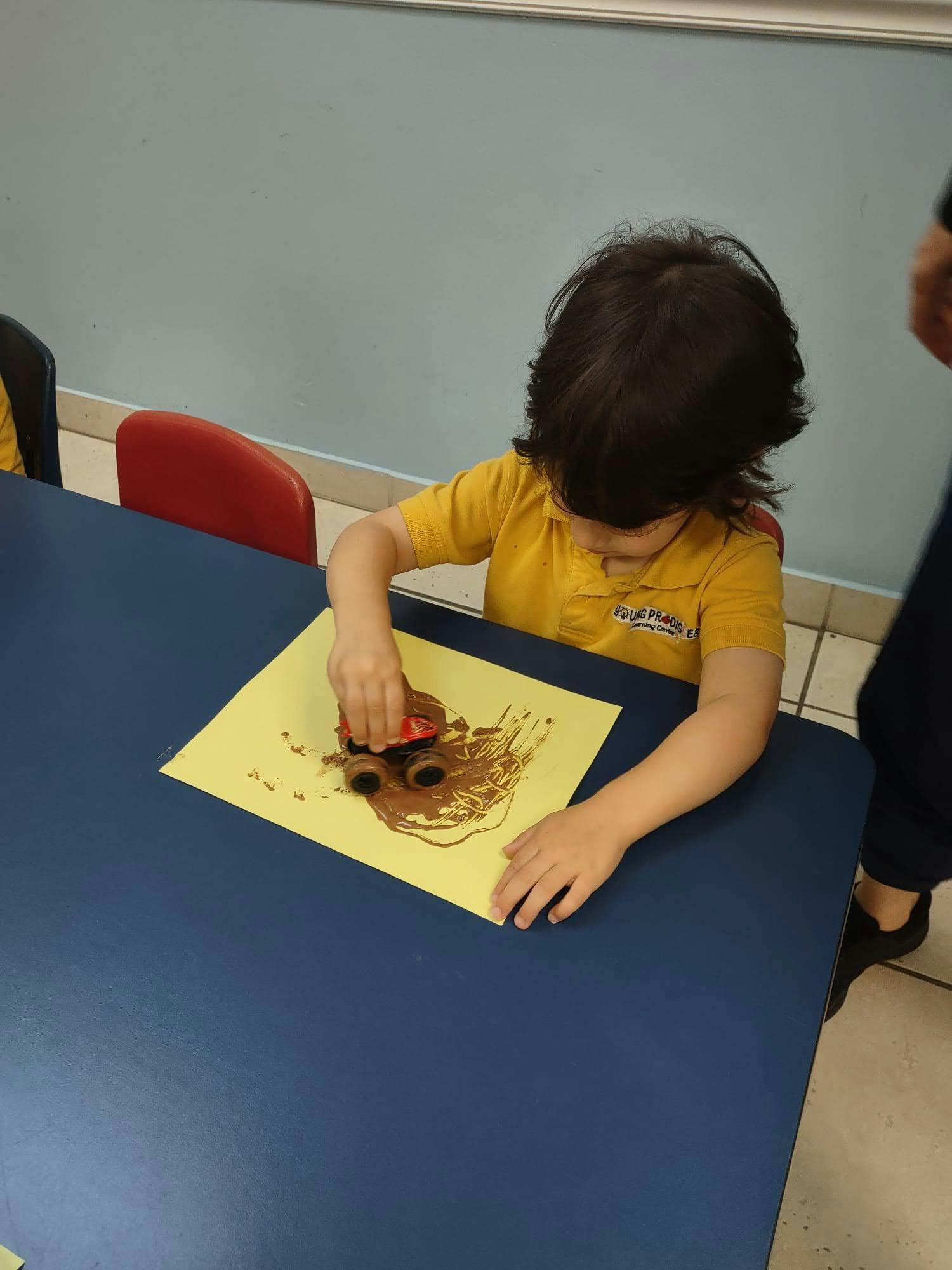 Child playing with a toy car on a yellow paper with brown paint