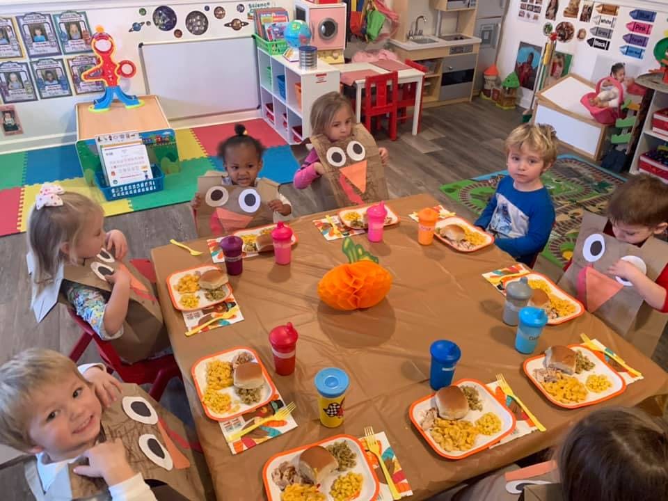 Children in turkey costumes sitting at a table with plates of food