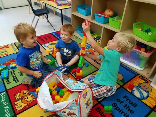 Three children playing with building blocks on a colorful rug