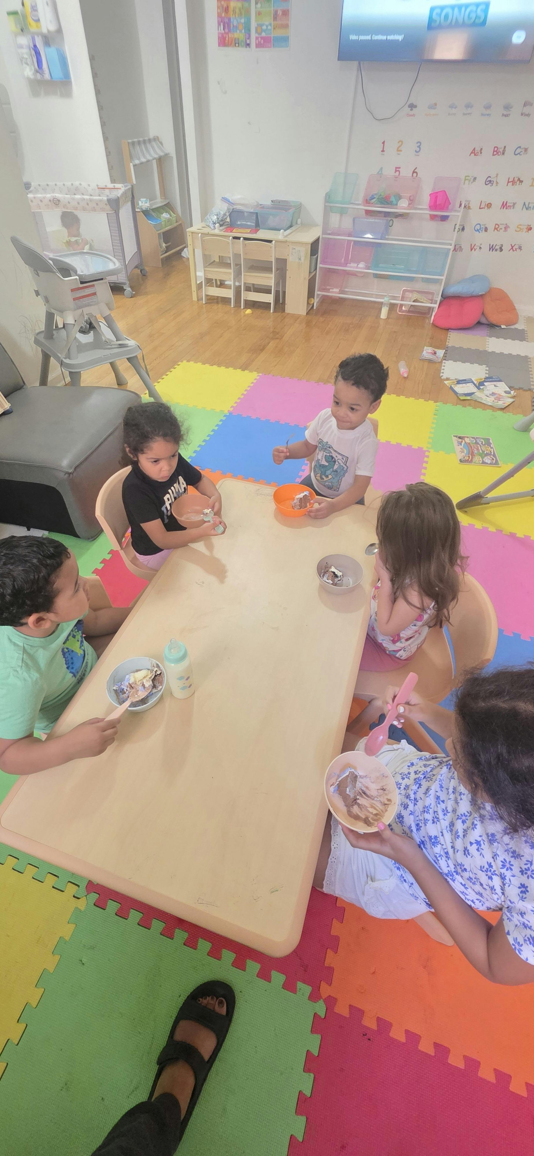 Five children eating from bowls at a table in a playroom