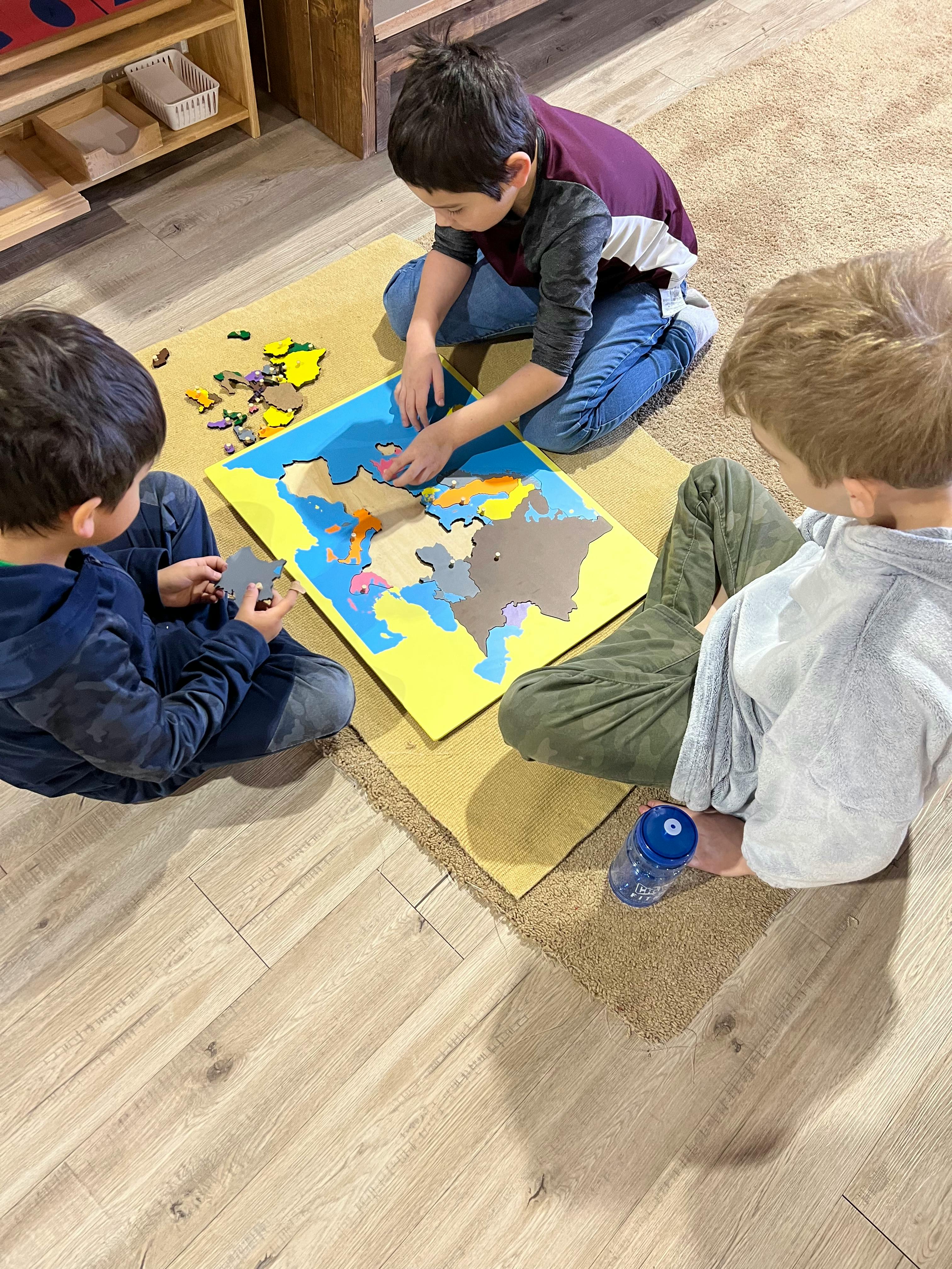 Three children on the floor assembling a large map puzzle